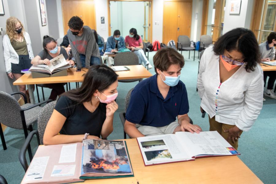 Three people leaning over open books on a table, in a library