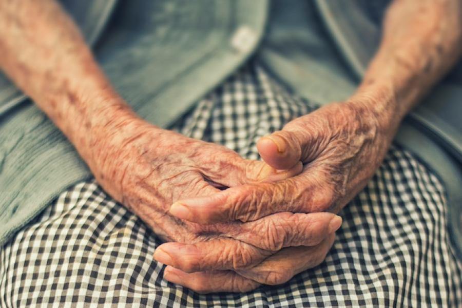 Hands of an elderly person clasped on a gingham print skirt