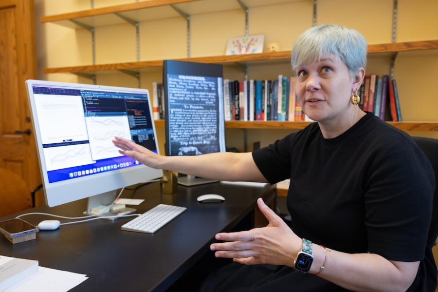 Person speaking while gesturing at a computer screen, showing graphs