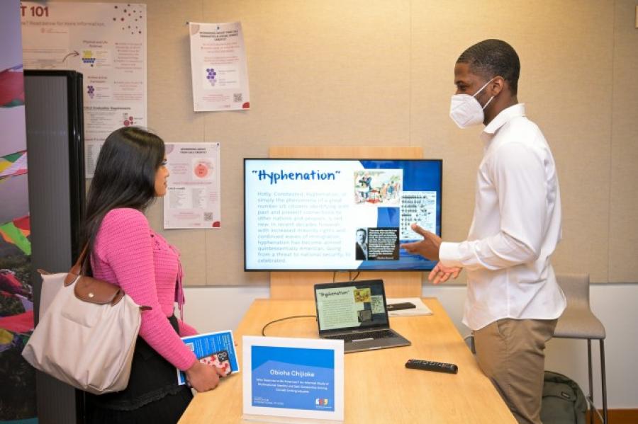 Two people converse over a table, with a computer screen at one end