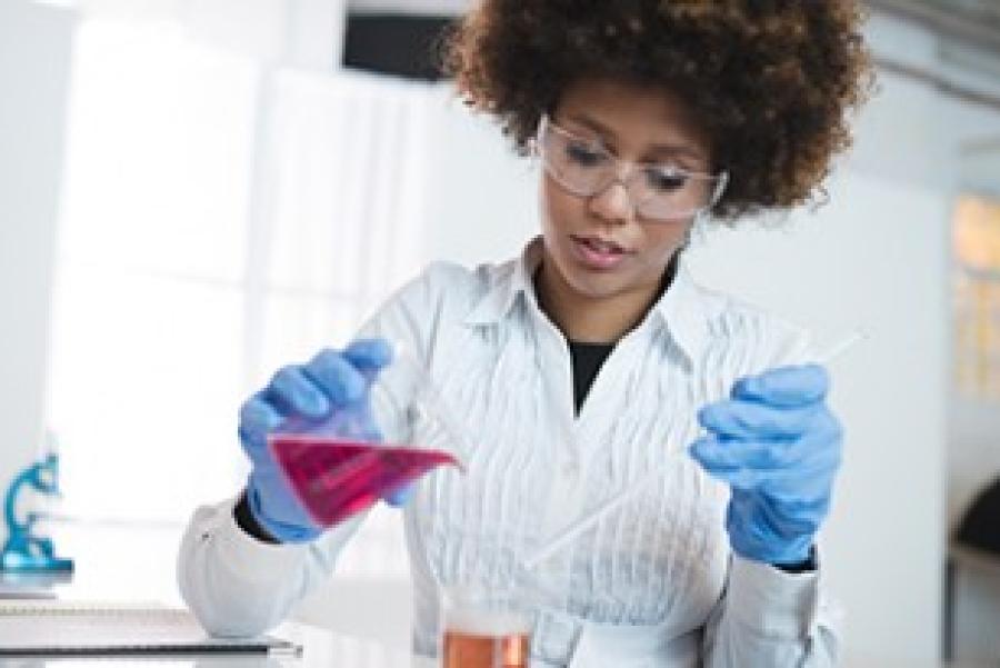 Person working in a chemistry lab, pouring colored liquid from one beaker to another