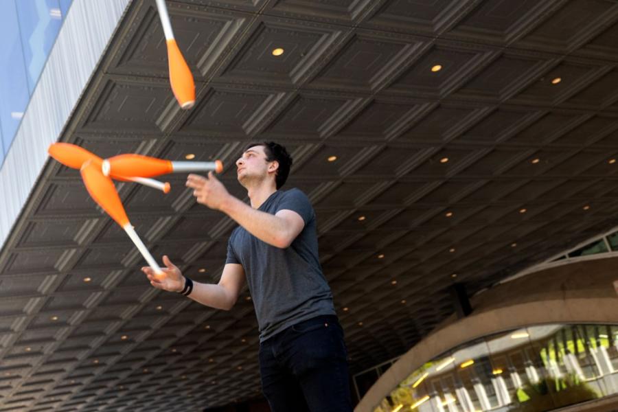 Person juggling four orange clubs under a dark overhang