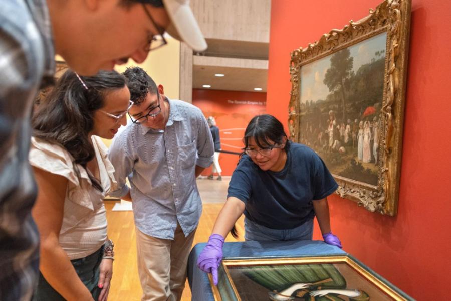 Four people cluster around a painting, laid out on a table