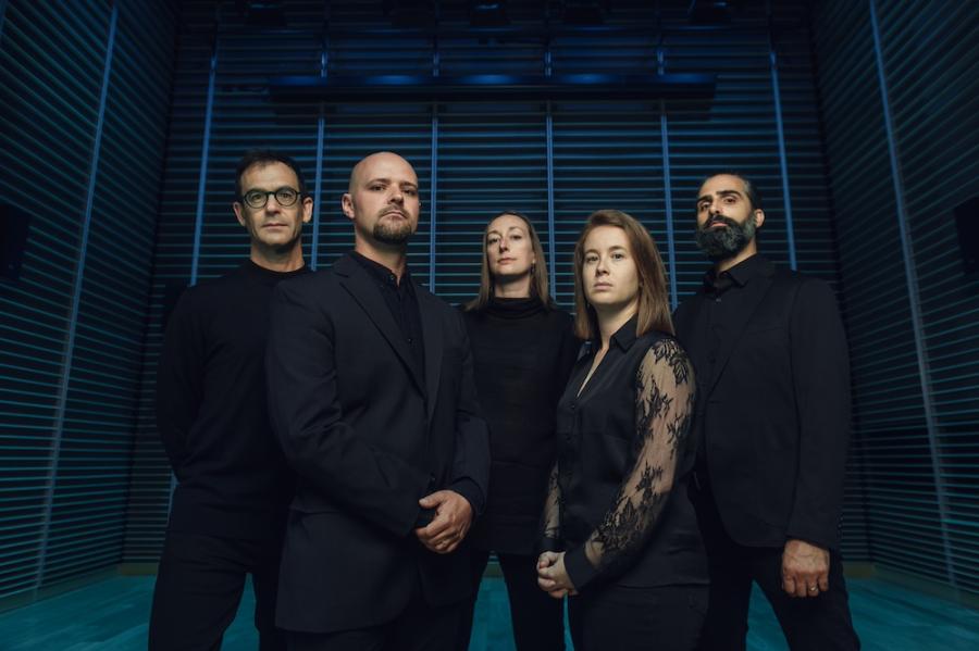 Five people wearing black pose against a blue and black background. They look forboding.