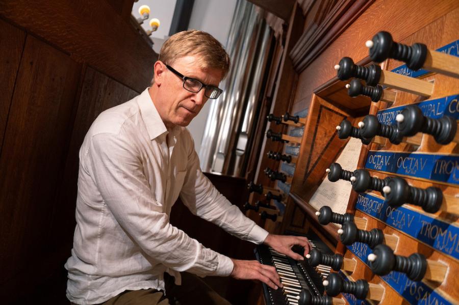 Person sitting at the consol of a wooden organ, hands on keyboard