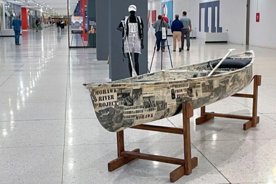 A canoe covered in written messages, in an exhibit hall