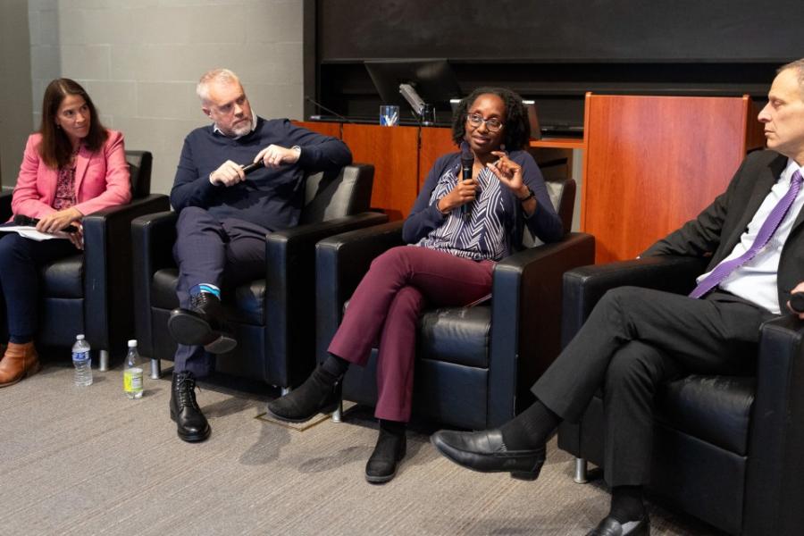 The panelists sitting in arm chairs, all three looking at Prof. Jamila Michener talking into the microphone.