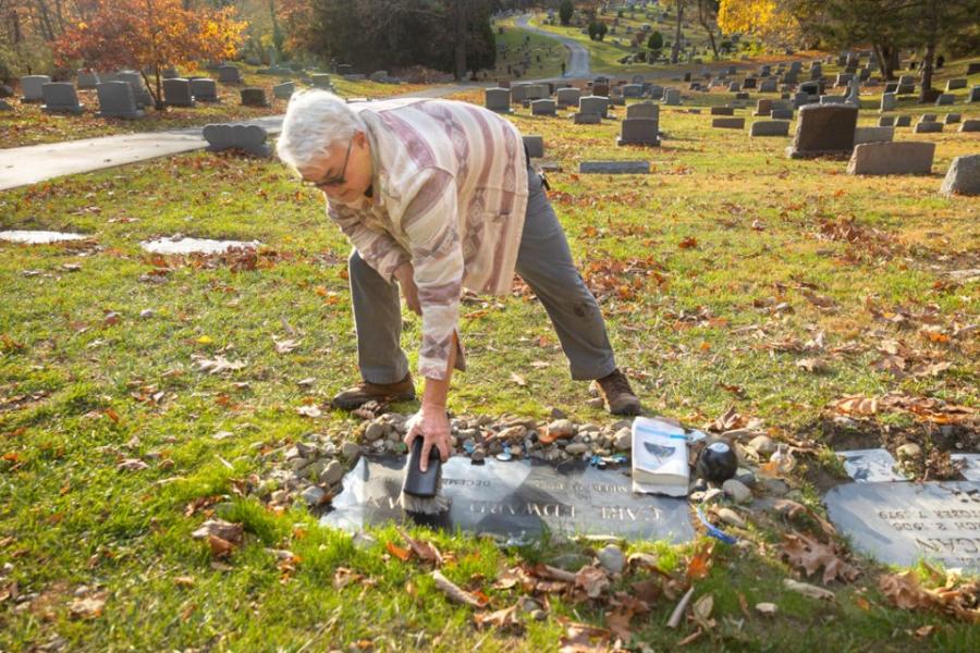 Person bending over to sweep a flat grave marker