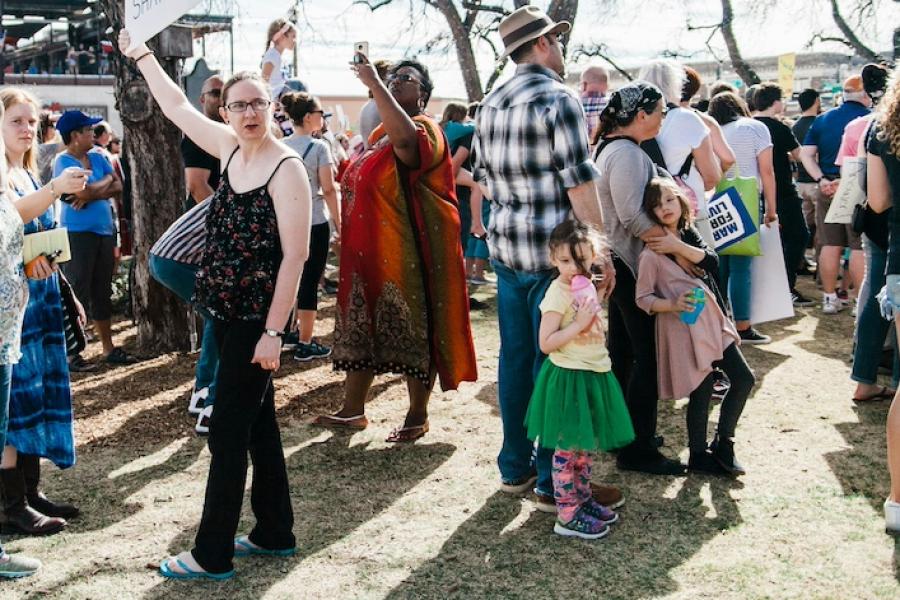 Dozens of people standing on a lawn, at a public rally