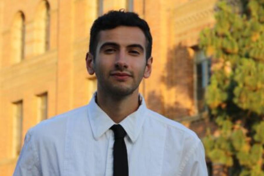 Jeremy Peschard Pórtela with white shirt and black tie, a faint beard and mustache, in front of a sunlight building.