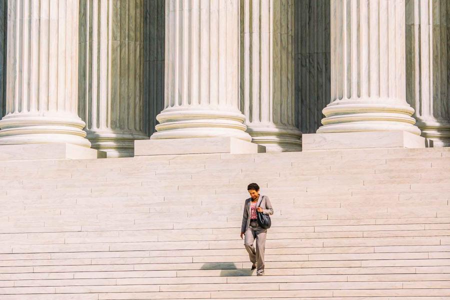 Woman in business clothes walking down the steps of the Supreme Court with the tall columns behind her.