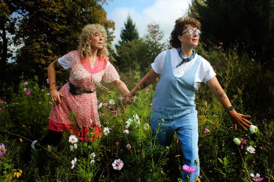 Two people -- characters in a play -- stand in a field full of flowers