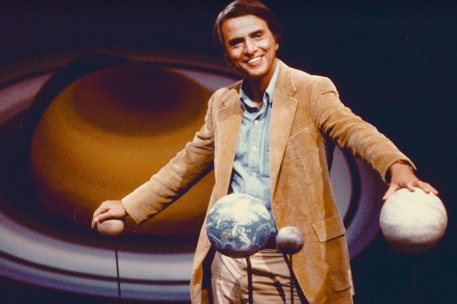 Person in late-70s chic tan sport coat, touching models of planets