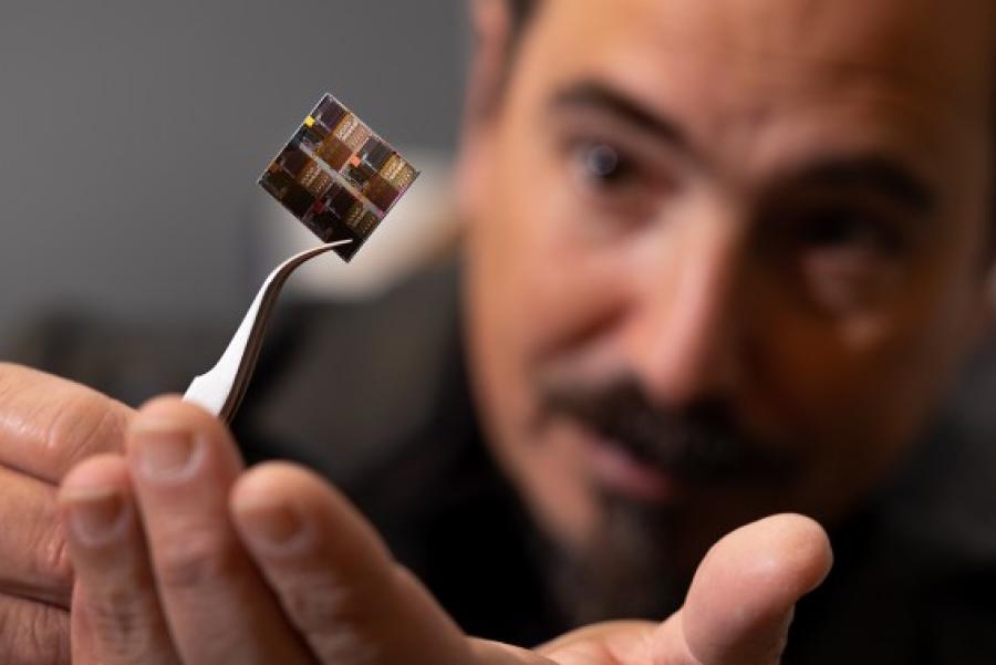 Pair of tweezers holding a tiny square of material; the person holding the tweezers looms in the background