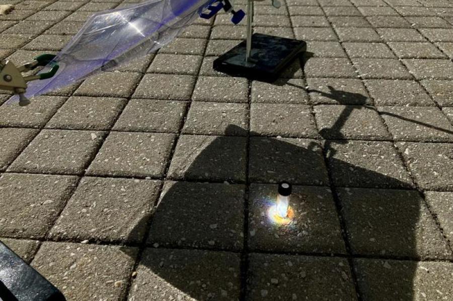 A glass vial sits in a patch of sunlight on a square tiled floor, with shadow around it.