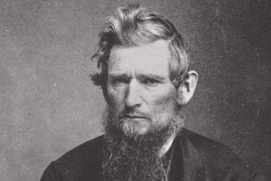 Black and white historic photo of Ezra Cornell, frowning and holding a pen. 