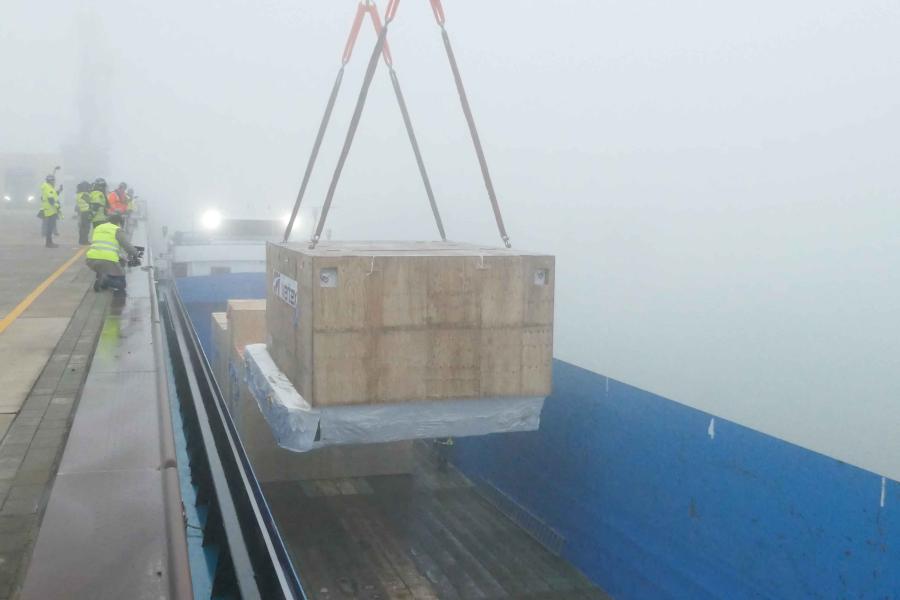 Huge crate suspended by ropes with people standing next to it.