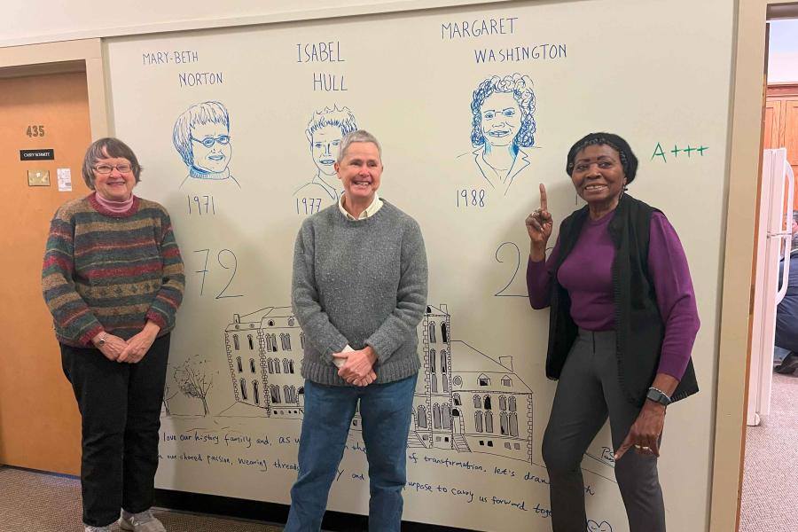 Mary Beth Norton, Isabel Hull and Margaret Washington, all smiling, standing in front of the drawings of their faces on the wall