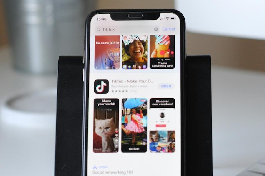 smart phone on a stand on a desk, showing TikTok home page