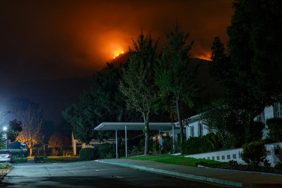 A house and garden in the foreground at night, with a wildfire glowing over a nearby hill