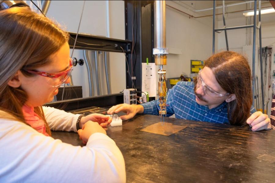 Three people wearing lab safety glasses look at a small scientific device