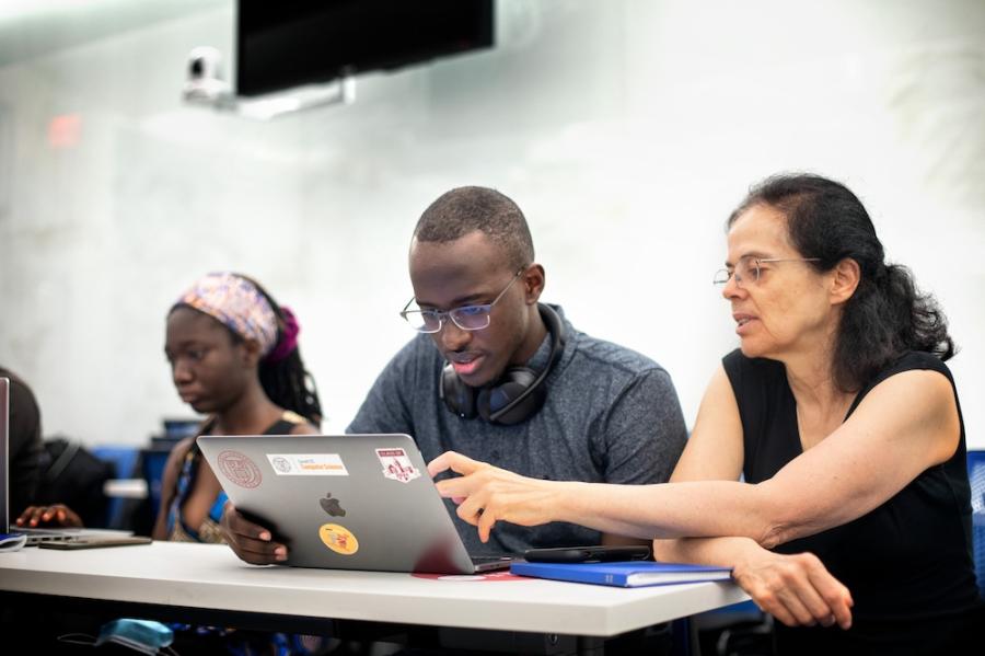 Two people look at a computer screen. One, an instructor, points at something