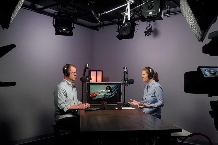 Two people sit at a table in a recording studio