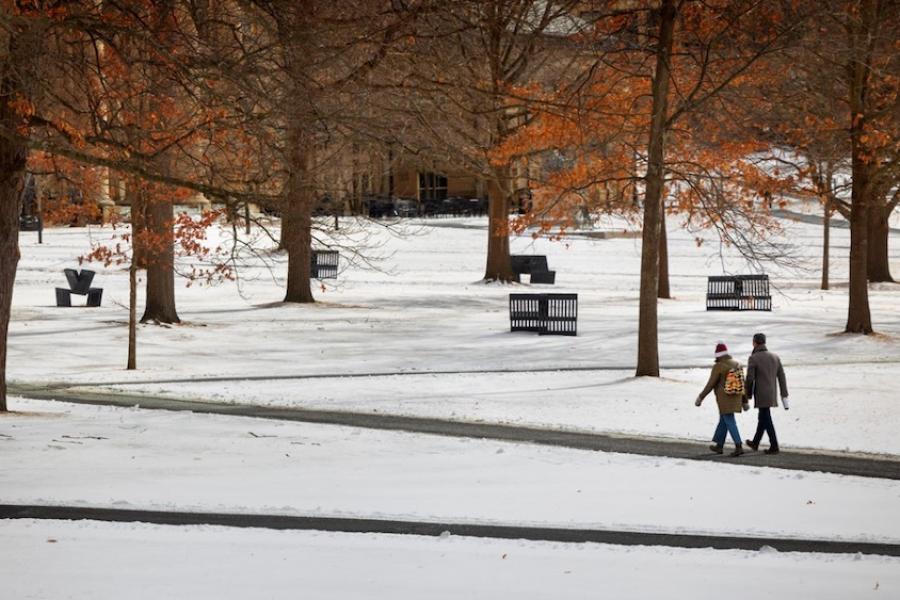 Two people walk across a snowy college quad