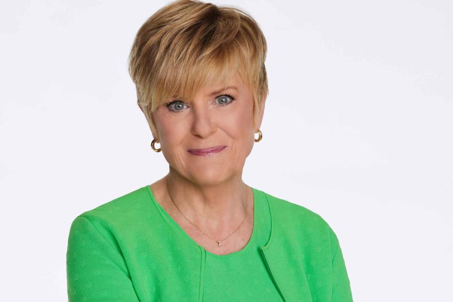 Anne Thompson in green, long-sleeved dress with arms crossed, smiling.