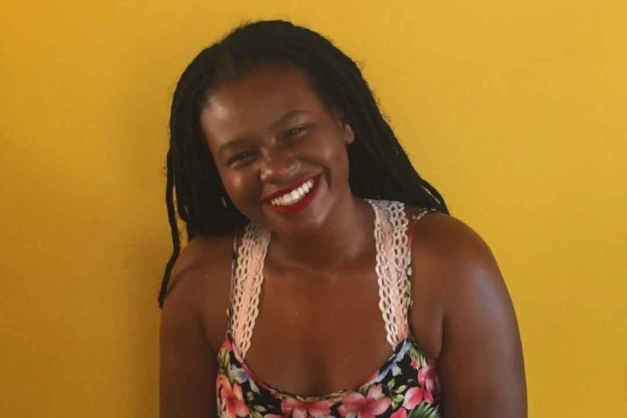 Brittani Samuel, head tilted to the right, smiling broadly, with long hair in small tight braids, wearing a flowered sleeveless dress