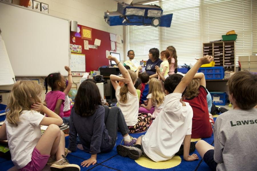 Several children sit on a rug in a classroom