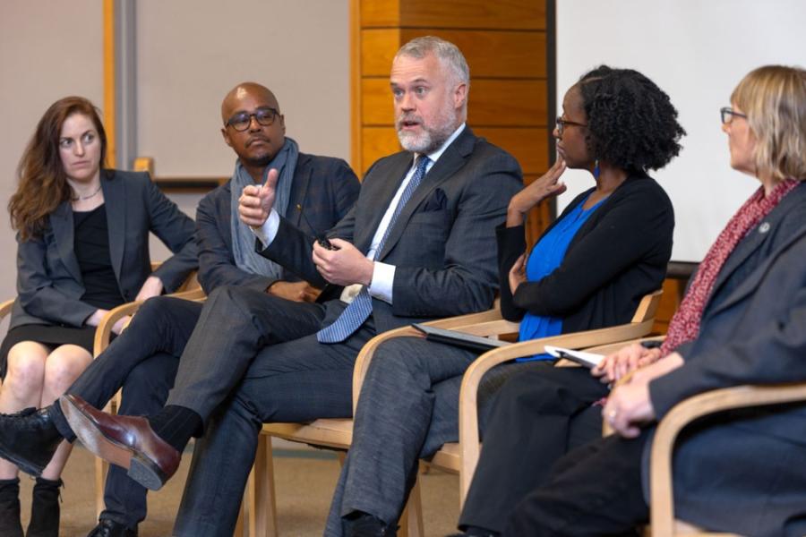 Six people sit in a row, during a panel discussion event