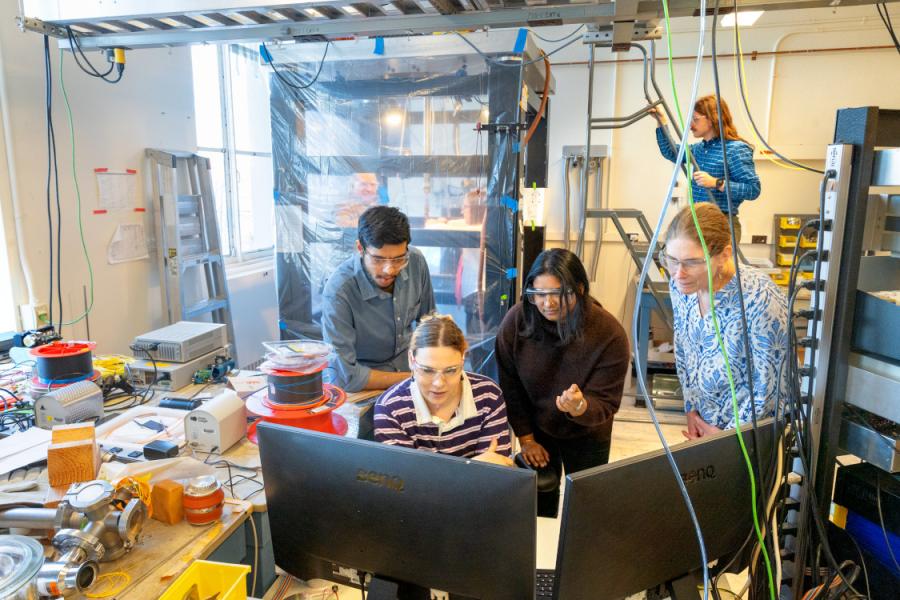 Three people cluster around a computer in a science lab