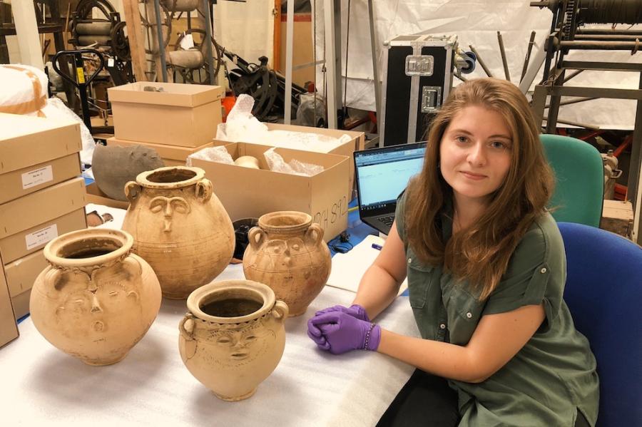 Person wearing laytex gloves sitting at a table with four ancient artifacts: pots