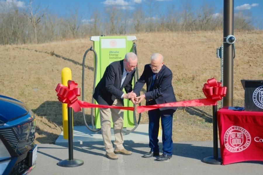 Two people cutting a red ribbon ceremonially. They are outdoors