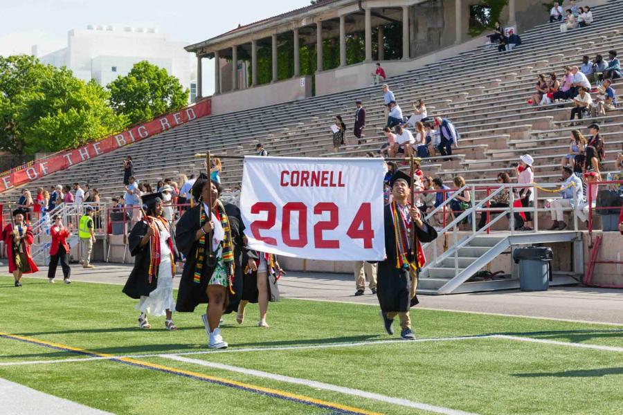 students carrying banner at graduation reading Cornell 2024