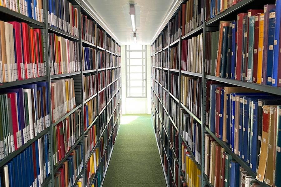 Looking through floor to ceiling book shelves in a library, toward a bright window