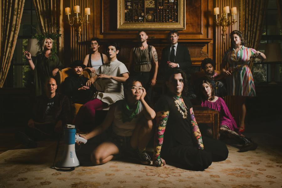 about a dozen people in creative clothing sit in a richly decorated room