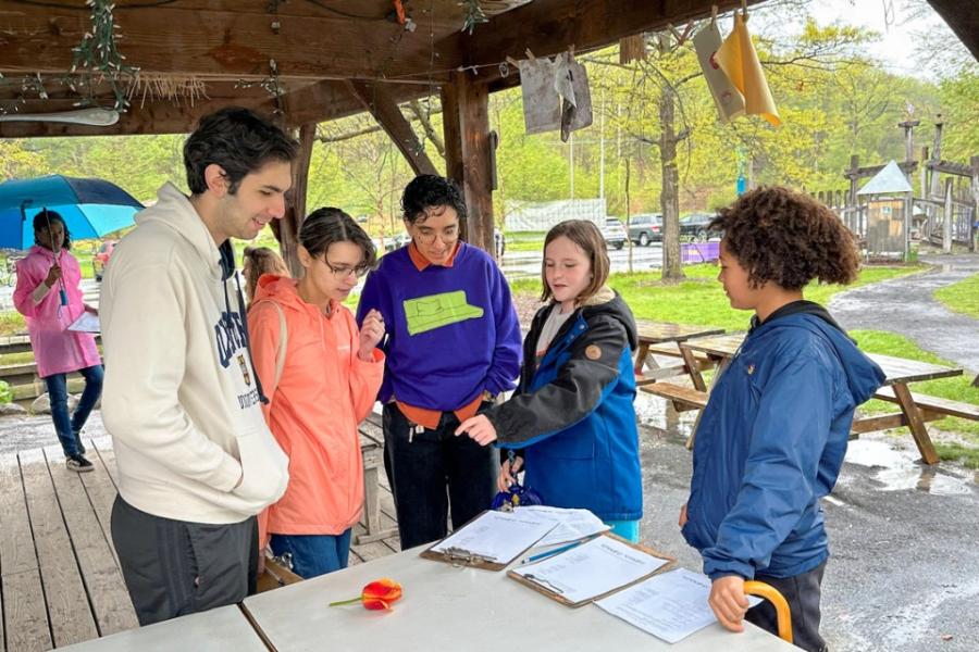 People cluster together in an outdoor shelter, looking at papers and flowers