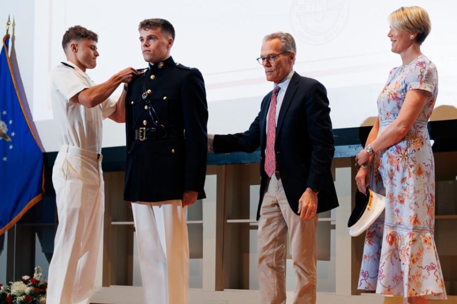 People on a stage; one in military uniform stands at attention