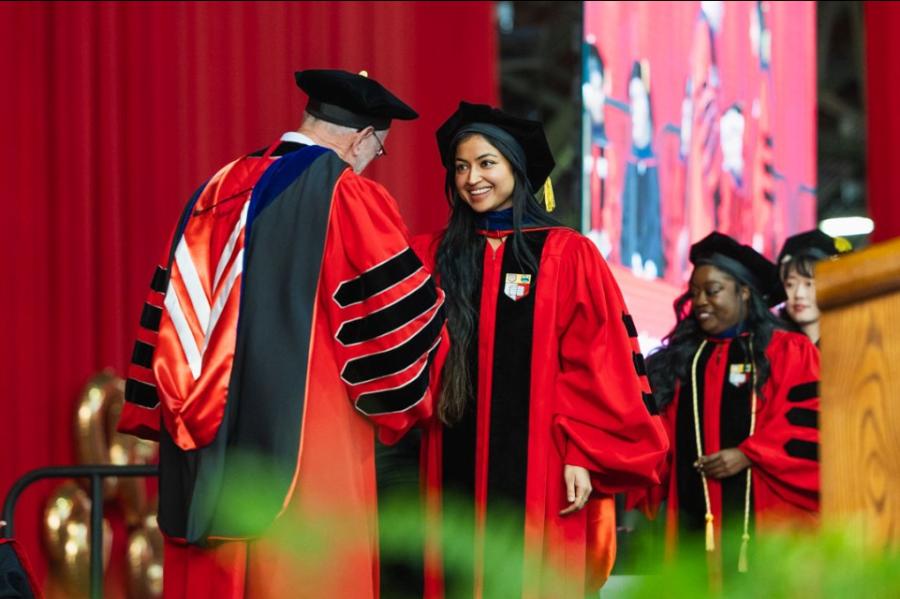 Person in academic robes shakes the hand of another person in academic robes