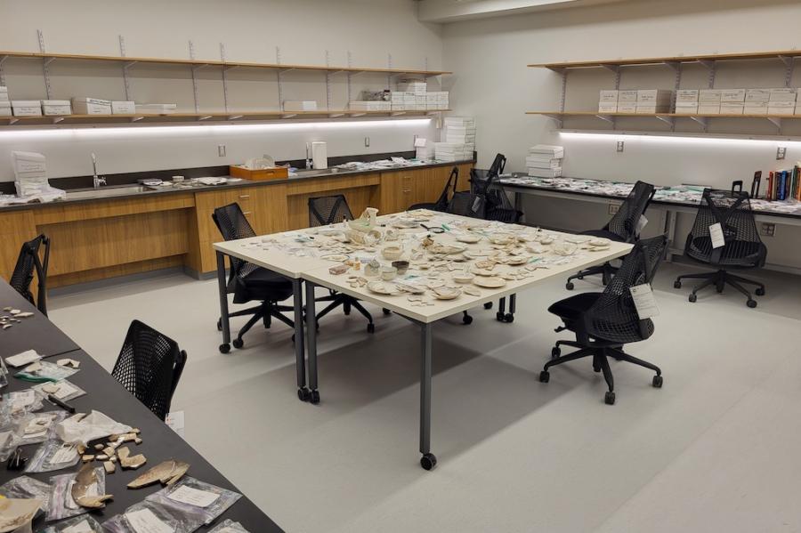 Large room dominated by a table covered with pieces of ceramic plates and bowls