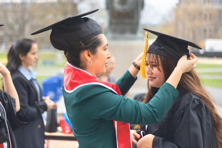 One person wearing graduation cap helps another with hers