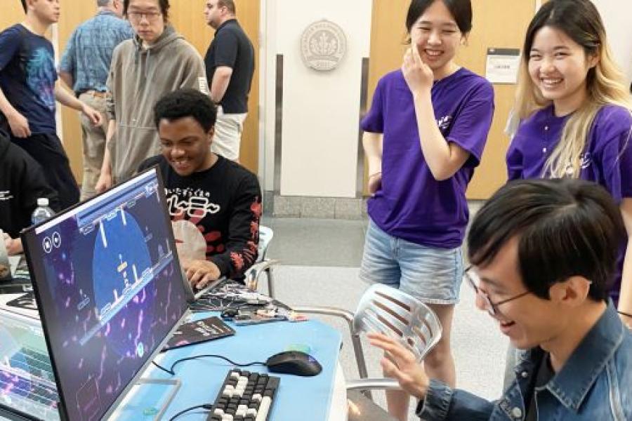 Several people in a room, laughing, with a video game on a large screen