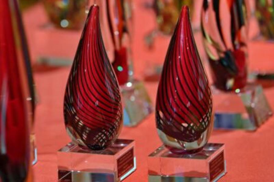 Glass figures shaped like a teardrop on top of a square glass base, red with black lines swirling down in parallel