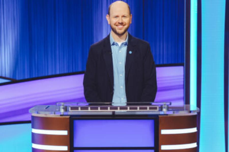 Dan Moren, mostly bald with a beard and a smile, standing at the Jeopardy podium with the word "Dan" on it