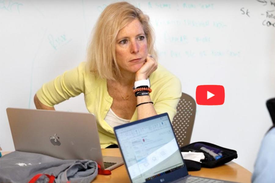 person at a desk with computers, looking thoughtful