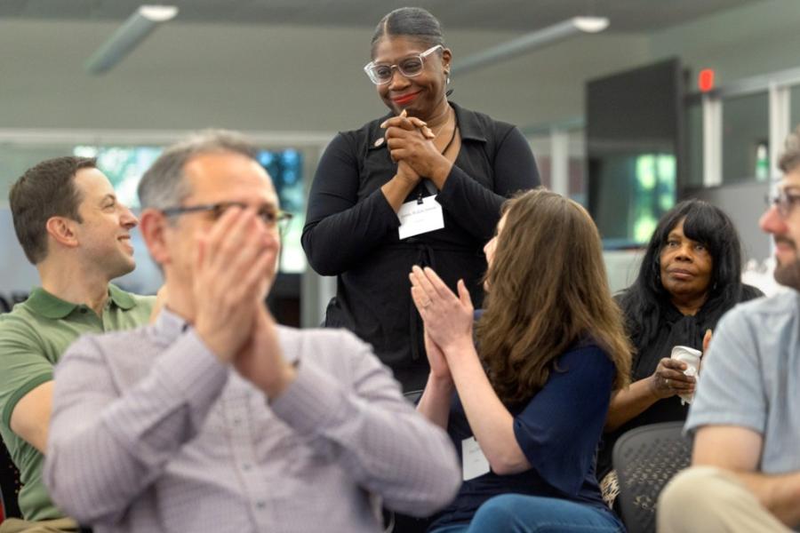 People in an audience applaud one person standing