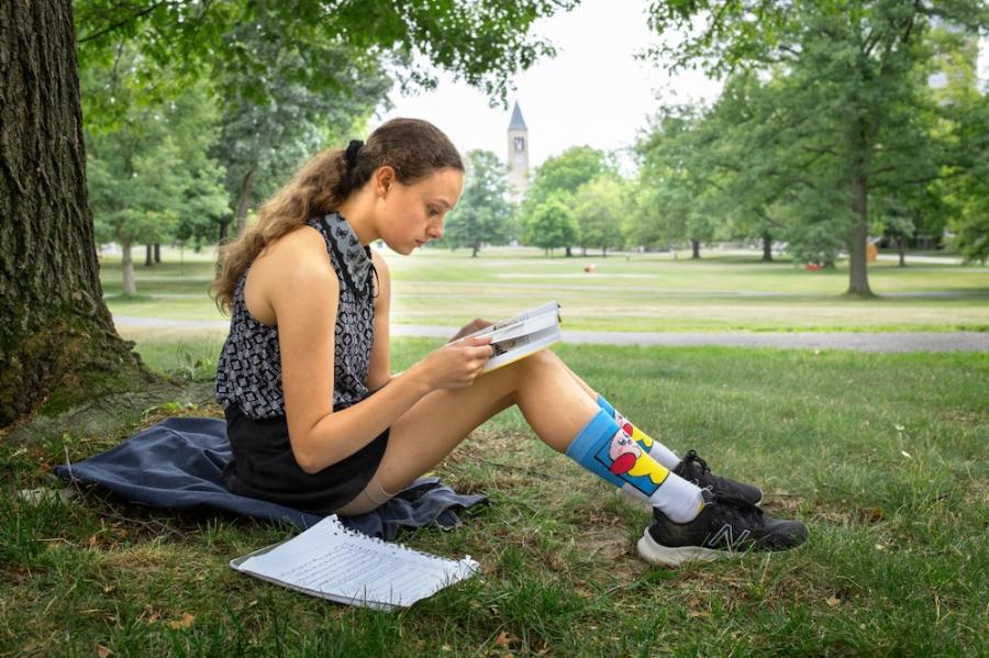 Person sitting on grass, reading a book propped on knees
