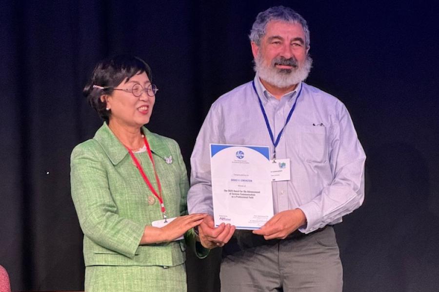 Two people standing on a stage, holding a certificate between them